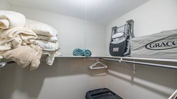 Une petite salle de bain compacte avec un espace de douche blanc, un porte-serviettes avec des serviettes pliées, un siège de douche noir et portable, et un sac étiqueté « GRACCO » accroché au mur.