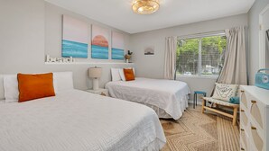 Une chambre d’hôtel avec deux lits, une petite table, une chaise, une lampe et des œuvres d’art accrochées au mur.