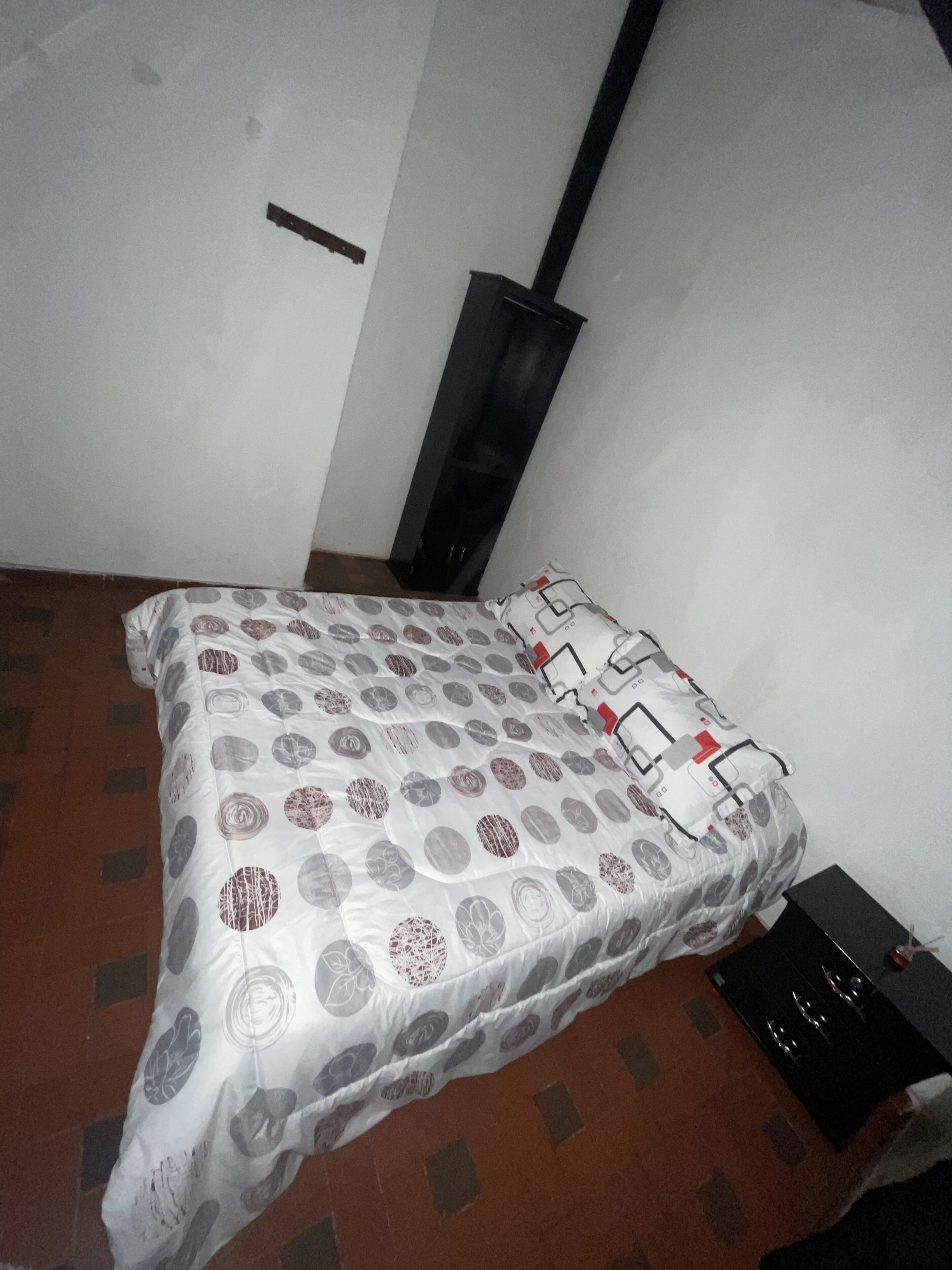 Ein Schlafzimmer mit einem Bett, einem schwarzen Heizkörper und einem kleinen Tisch mit einem schwarzen Gegenstand darauf.