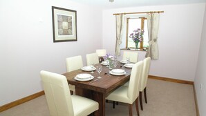 A dining room with a wooden table set for six, white chairs, a vase with flowers, and a framed picture on the wall. - Wheelhouse Cottage Longstone Holiday (Sneatonthorpe near Whitby)