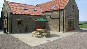 A stone building with a red-tiled roof, a wooden door, and a small patio with a table and benches. - Wheelhouse Cottage Longstone Holiday (Sneatonthorpe near Whitby)