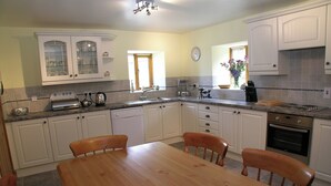 A kitchen with white cabinets, a wooden dining table, and a built-in oven. - Wheelhouse Cottage Longstone Holiday (Sneatonthorpe near Whitby)