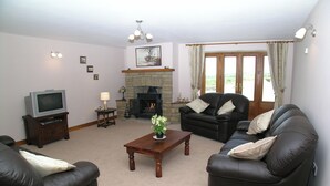 A living room with a fireplace, two sofas, a coffee table, and a television. - Wheelhouse Cottage Longstone Holiday (Sneatonthorpe near Whitby)