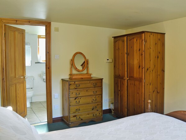 A bedroom with a wooden dresser, a wardrobe, a bed, and a bathroom visible through an open door.