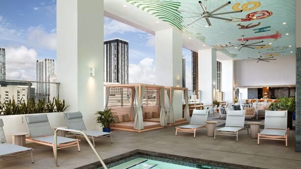 Un área de piscina en la azotea con sillones de descanso, un rincón de estar con una planta y vistas a edificios altos.