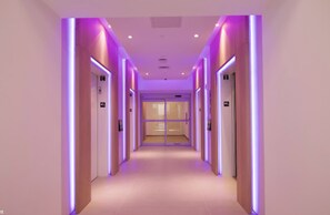 A hallway with doors on both sides, illuminated by purple lighting.