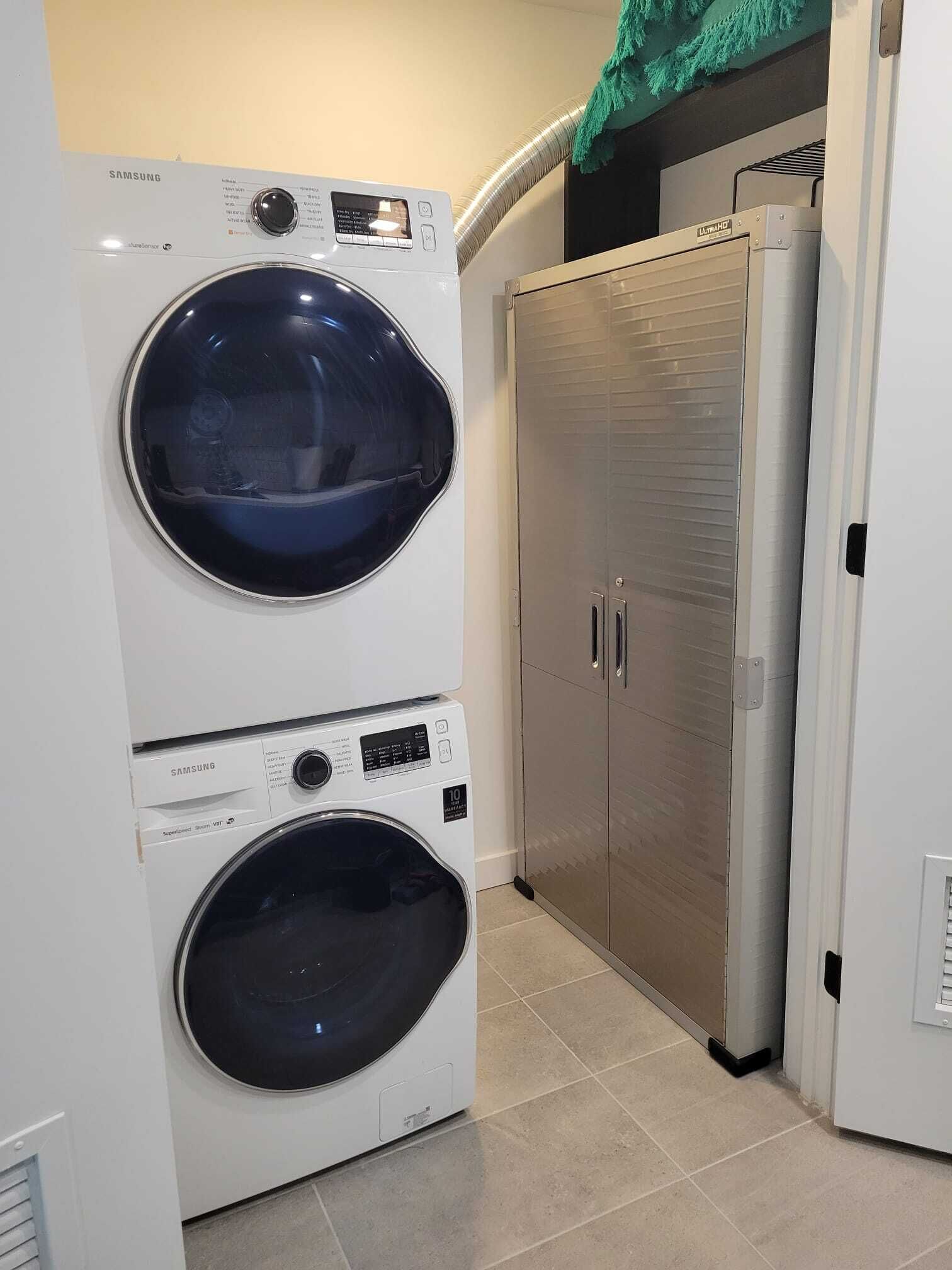 A laundry room with two stacked Samsung washing machines and a stainless steel refrigerator.