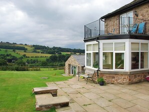 A stone house with a balcony, a small garden, and a view of the countryside.