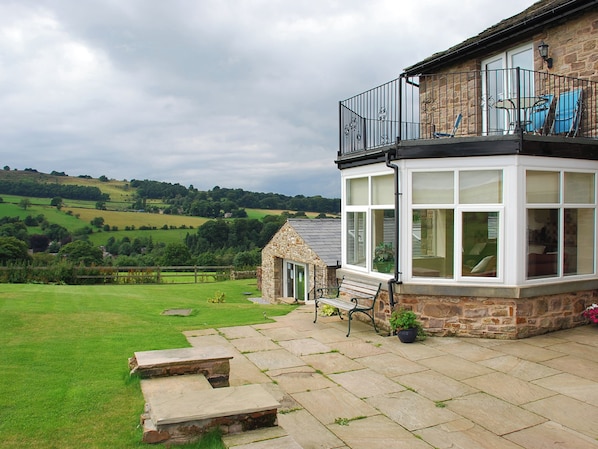 A stone house with a balcony, a small garden, and a view of the countryside.