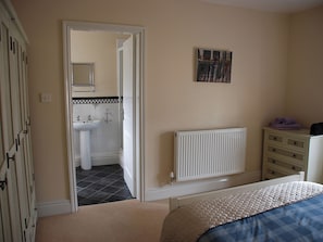 A bedroom with a bed, a radiator, a dresser, and a bathroom visible through an open door.