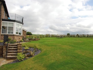 A stone house with a large glass window, a grassy yard, and a wooden fence.