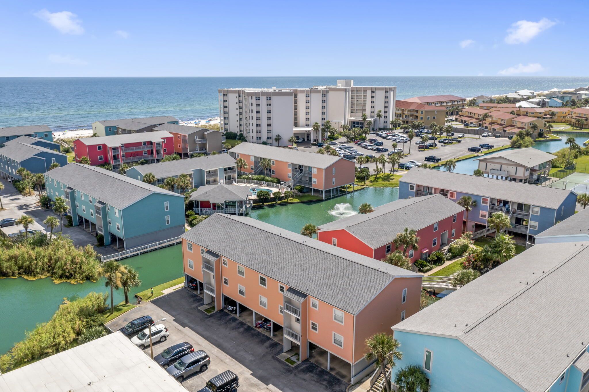 A coastal hotel with multiple buildings, a parking area, and a swimming pool.