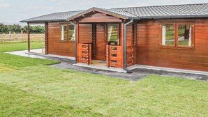 A wooden cabin with a porch, a door, and windows. - 2 bedroom accommodation in LLANFAIRPWLLGWYNGYLL (LLANFAIRPWLLGWYNGYLL)