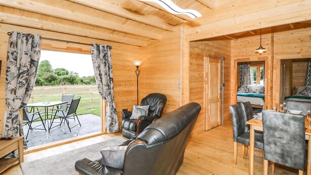 A wooden interior with a sofa, chairs, a dining table, and a view of the outdoors. - 2 bedroom accommodation in LLANFAIRPWLLGWYNGYLL (LLANFAIRPWLLGWYNGYLL)