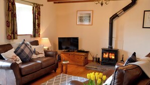 Una sala de estar acogedora con un sofá de cuero marrón, un televisor, una chimenea y un jarrón con tulipanes amarillos.