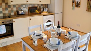 Una cocina con armarios blancos, microondas, refrigerador, lavamanos y una mesa de comedor con platos, tazones y cubiertos.