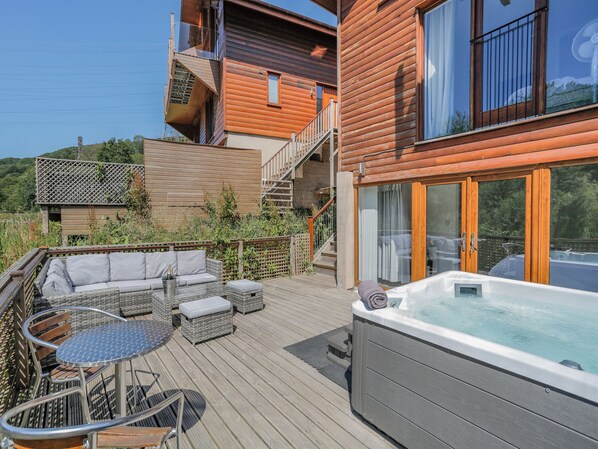 A wooden deck with outdoor furniture, a hot tub, and a staircase leading to an upper level.