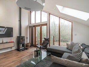 Ein modernes Wohnzimmer mit Flachbildfernseher, Kamin, Glastisch und einer Couch mit gemusterten Kissen.