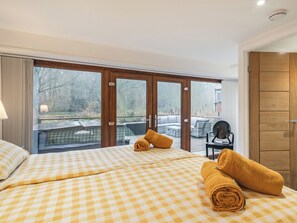 A hotel room with a checkered bedspread, a view of a deck with outdoor furniture, and a wooden door.
