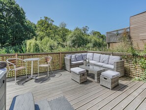 A deck with outdoor furniture, including a sofa and chairs, surrounded by a wooden fence and lush greenery.