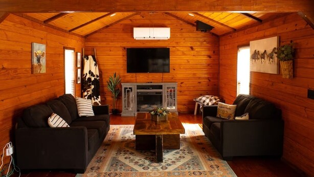 A cozy log cabin interior with two sofas, a coffee table, a fireplace, and a TV mounted on the wall. - Charming Cabin + Pond View + Hot Tub (Carthage)