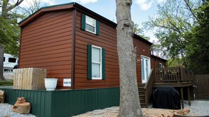 A cabin with a green exterior, a deck, and a sign indicating it is Cabin 03. - Charming Cabin + Pond View + Hot Tub (Carthage)
