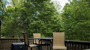 An outdoor deck with wicker chairs and a table, surrounded by trees. - Charming Cabin + Pond View + Hot Tub (Carthage)
