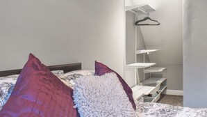 Une chambre à coucher avec un lit, des oreillers, une armoire suspendue et un mur blanc.