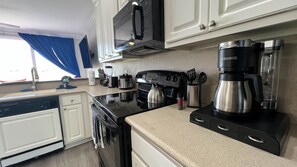 A modern kitchen with white cabinets, a black stove, a kettle, a coffee maker, and a dishwasher. - Perfect family two story Villa 8 near SeaWorld (Orlando)
