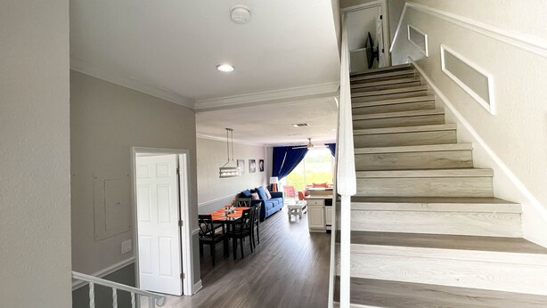 A spacious living area with a dining table and chairs, a staircase, and a view of the outdoors.