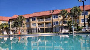 A swimming pool with a clear view of a multi-story building with balconies and a red-tiled roof.
