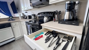 A kitchen with white cabinets, a black stove, a coffee maker, and various utensils in a drawer.