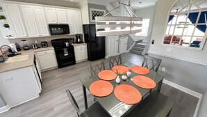 A modern kitchen with white cabinets, a black refrigerator, and a dining area with a glass table and orange placemats.