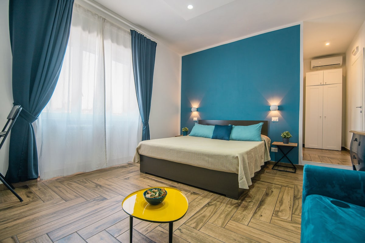Un dormitorio con una cama, una mesita con un cuenco, una pared azul y un armario.