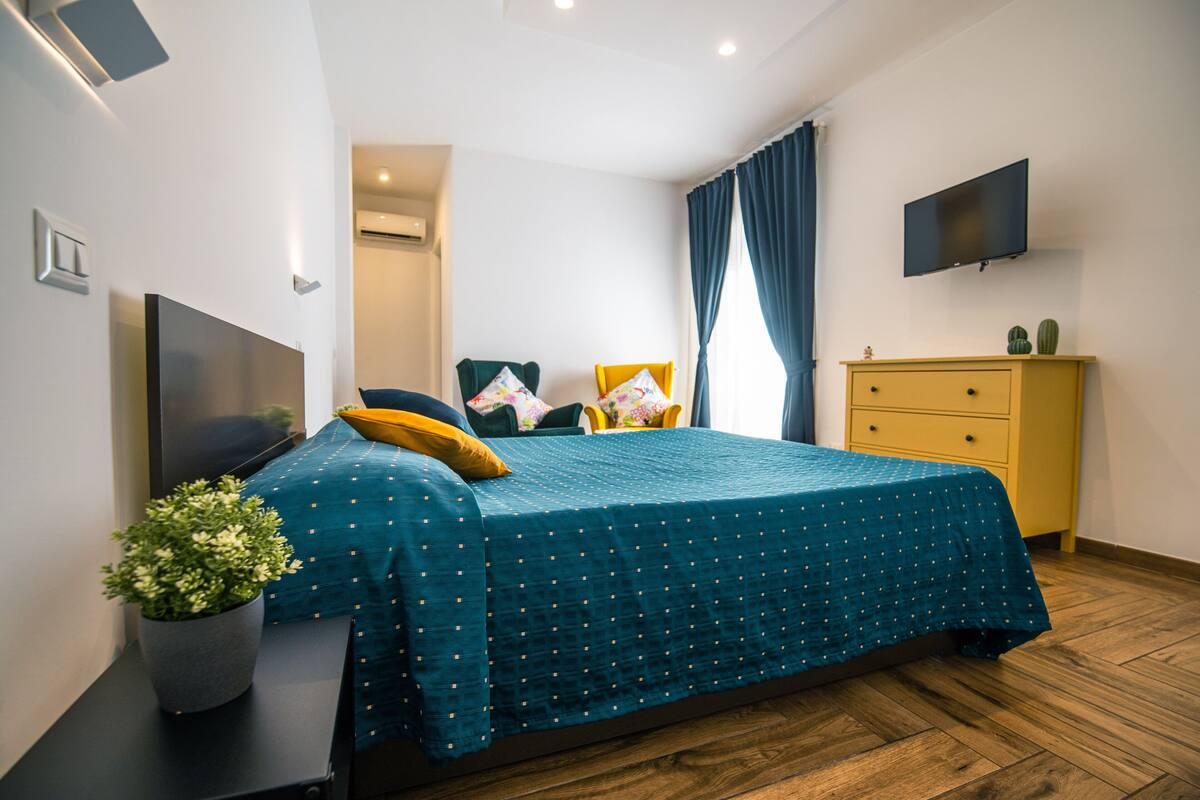 Un dormitorio moderno con cama, televisor, cómoda y planta en maceta.