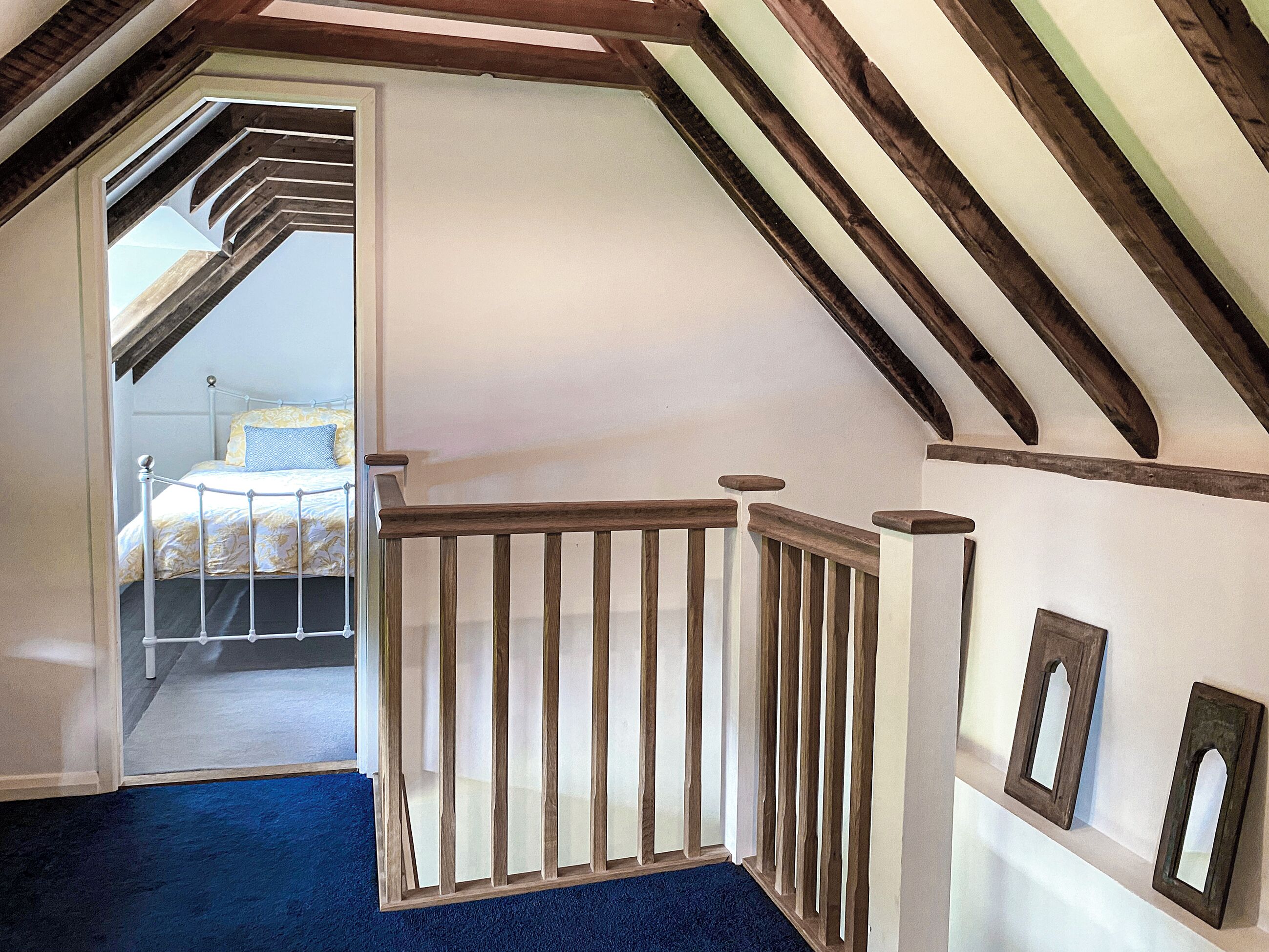A bedroom with a sloped ceiling, a wooden railing, and a bed with a patterned bedspread.