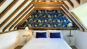 A bedroom with a sloped ceiling, a floral-patterned wall, a bed with white and blue bedding, and two bedside tables with lamps.