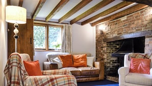 A cozy living room with a brick fireplace, a sofa with orange cushions, and a plaid throw blanket.
