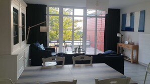 Un área de comedor con una mesa y sillas, un sofá, una ventana con vistas al exterior y una lámpara.