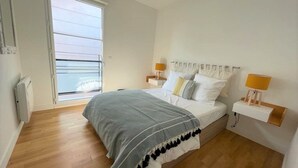 Un dormitorio con cama, lámparas de noche, una ventana y una mesita de noche.