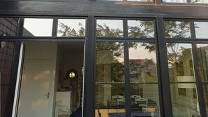 Un edificio moderno con grandes ventanales y un espacio interior visible, que incluye un área de comedor con mesas y sillas.