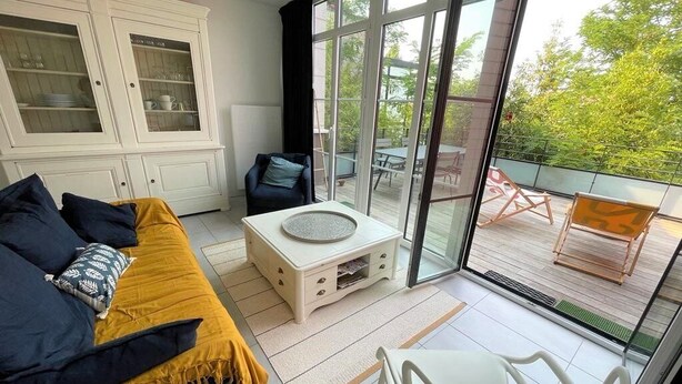 Habitación con sofá, una mesita, un armario y vista a un patio exterior con sillas.