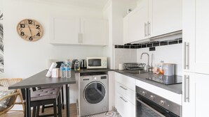 Une cuisine compacte avec des meubles blancs, un four à micro-ondes, un évier et un lave-linge.