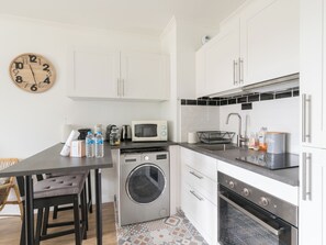 Una cucina funzionale con lavatrice, forno a microonde, lavello e orologio a parete.