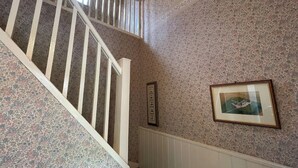 A staircase with white railings leading to a landing with a floral-patterned wall and a framed picture. - Birch Cottage - UK38992 (Dalcross)