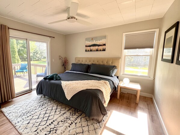 Un dormitorio con una cama grande, un ventilador de techo, una ventana con persianas y vistas al exterior.