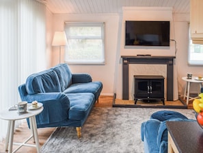 Una sala de estar con un sofá azul, una chimenea, un televisor montado arriba y una mesita con una taza.