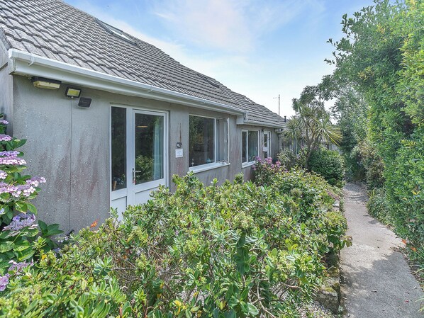 A residential building with a tiled roof, a pathway leading to the entrance, and lush greenery surrounding the property.