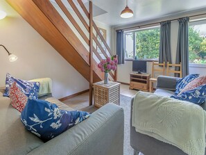 A living room with a wooden staircase, a television, and a view of greenery outside.