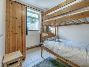 A bunk bed room with a wooden floor, a window, a radiator, and a small table.